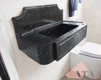 May include: A black marble bathroom sink with a decorative, curved top and a rectangular basin. The sink is mounted on a white wall.