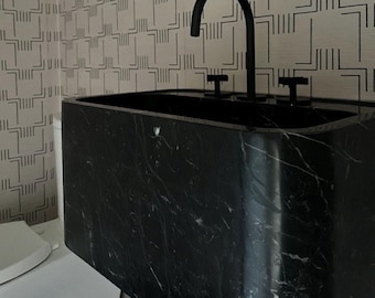 May include: A black marble bathroom sink with a black faucet and two handles. The sink is set against a white wall with a geometric pattern.