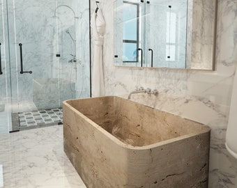 May include: A large, rectangular bathtub made of natural stone with a rough, textured surface. The bathtub is in a modern bathroom with white marble walls and a glass shower enclosure.