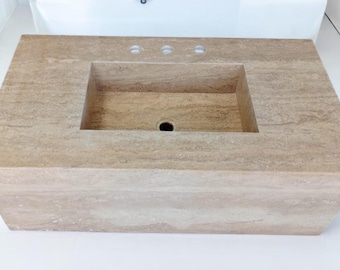 May include: A rectangular, beige stone bathroom sink with a built-in basin and three faucet holes. The sink has a natural, textured appearance and is designed for a modern bathroom.