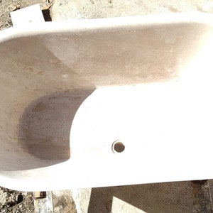May include: A white oval bathtub made of stone. The bathtub has a drain hole in the bottom.