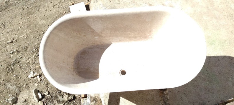 May include: A white oval bathtub made of stone. The bathtub has a drain hole in the bottom.