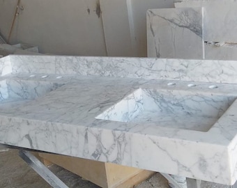 May include: A white marble double vanity sink with two rectangular basins. The sink is made of polished marble with a veined pattern.