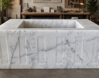 May include: A rectangular white marble sink with a recessed basin. The sink features vertical, grooved detailing on the front and sides. The marble has gray veining throughout, adding to its natural aesthetic. The sink is a modern bathroom fixture.