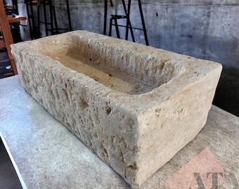 May include: A large, rectangular stone trough with a rough, textured surface. The trough is made of light beige stone and has a slightly rounded bottom.