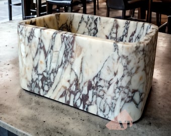 May include: A rectangular white marble sink with a unique veined pattern. The sink is made of natural stone and has a smooth, polished finish.