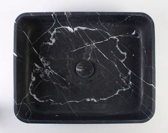 May include: A black marble vessel sink with a white veining pattern. The sink has a round drain hole in the center.
