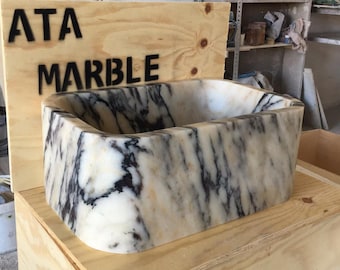 May include: A white marble sink with black veining, sitting on a wooden crate with the text "ATA MARBLE" printed on the side.