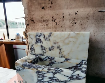 May include: A white marble sink with purple and gold veining. The sink is built into a white marble wall with purple and gold veining. The sink is rectangular and has a small ledge on the side.