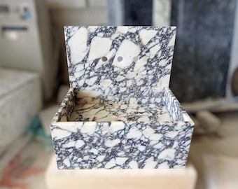 May include: A white and black marble sink with two holes for faucets. The sink is rectangular and has a raised backsplash.
