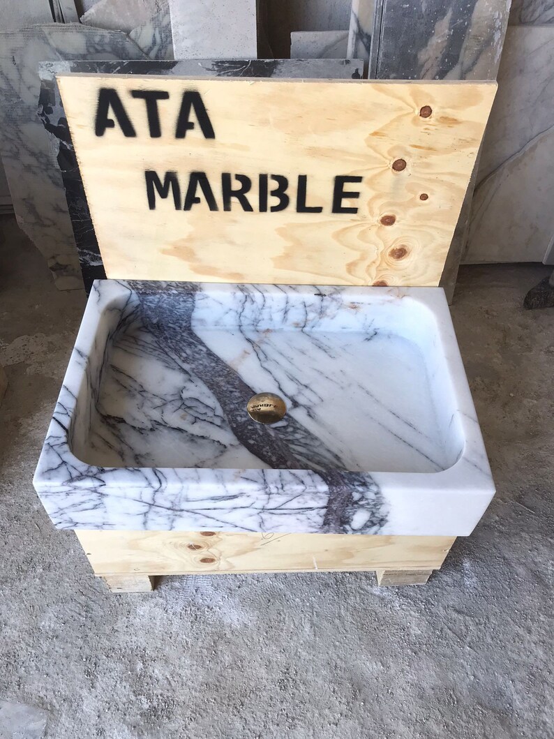 May include: A white marble sink with gray veining, set on a wooden base with the text "ATA MARBLE" on the side.