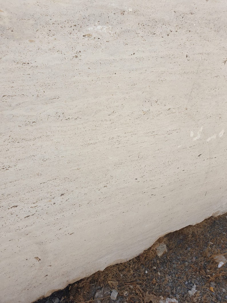 May include: A close-up of a large, light beige travertine slab with a smooth, polished surface. The slab has a natural, veined pattern and a slightly textured finish.