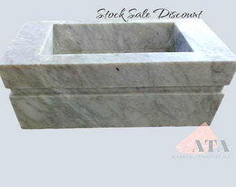 May include: A white marble sink with a rectangular shape and a raised lip around the edge. The sink is on a white marble base with a raised lip around the edge. The sink is made of natural stone and has a unique veining pattern.