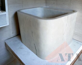 Può includere: Un grande lavabo rettangolare in marmo bianco con bordi arrotondati. Il lavabo è appoggiato su un piano di lavoro bianco.