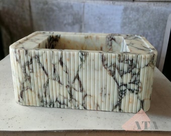 May include: A white marble rectangular sink with a decorative, ribbed design. The sink has a light brown and gray marbling pattern.