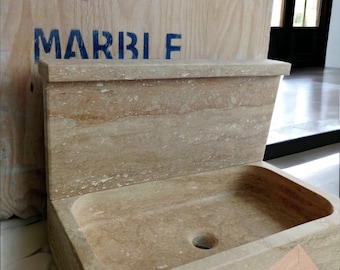May include: A beige travertine stone sink with a single drain hole. The sink is attached to a matching travertine stone backsplash. The backsplash has the word "MARBLE" written on it in blue paint.