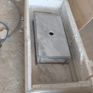 Puede incluir: Un lavabo de encimera de m&aacute;rmol blanco con un agujero para un grifo se est&aacute; instalando en un marco de madera. El lavabo est&aacute; rodeado de aislamiento de espuma blanca.