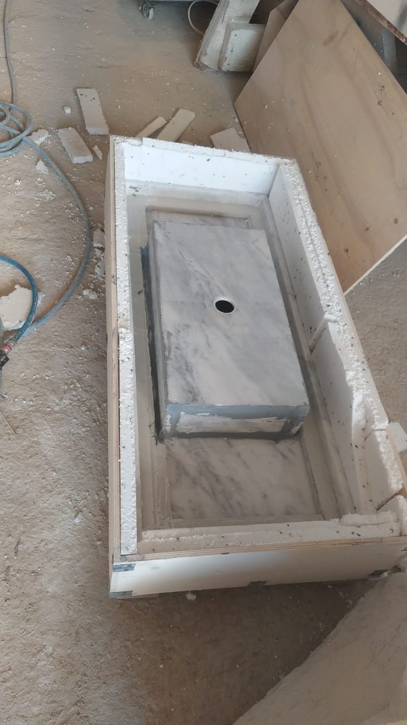 Puede incluir: Un lavabo de encimera de m&aacute;rmol blanco con un agujero para un grifo se est&aacute; instalando en un marco de madera. El lavabo est&aacute; rodeado de aislamiento de espuma blanca.