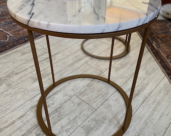 May include: Two round marble top side tables with gold metal frames. The larger table has a white marble top and the smaller table has a gray marble top.