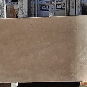 May include: A large, light brown, concrete planter with a rounded, oval shape. The planter is sitting on wooden blocks.