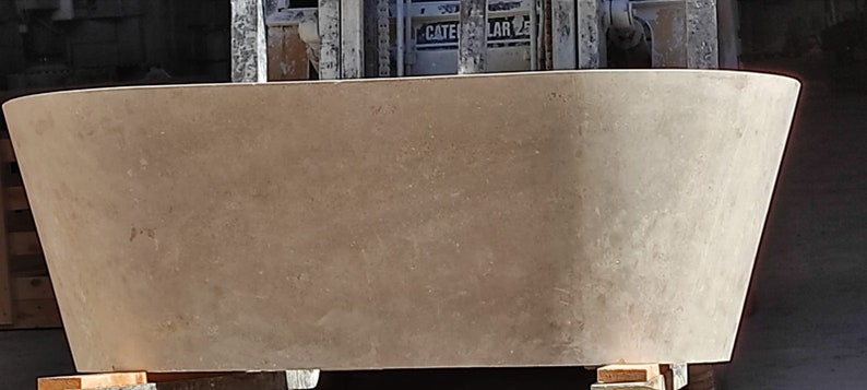 May include: A large, light brown, concrete planter with a rounded, oval shape. The planter is sitting on wooden blocks.