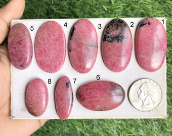 Puede incluir: Diez piedras preciosas ovaladas de color rosa y negro con los números del 1 al 8 impresos en una superficie blanca. Las piedras preciosas están dispuestas en dos filas.