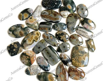 May include: A collection of polished gemstones in various shapes, including ovals and rectangles. The stones display a mix of colors, such as green, brown, and gray, with unique patterns and textures. The image is from AuroraGemsCo.