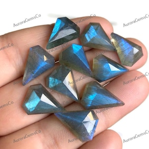 May include: A collection of ten faceted labradorite gemstone cabochons in shades of gray and blue with iridescent flashes. The stones are shaped like a teardrop with a pointed tip and a flat base.
