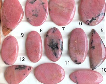 May include: A collection of twelve polished rhodonite gemstones in various shapes, including oval, teardrop, and irregular forms. The stones display a vibrant pink hue with black veining and inclusions, showcasing natural patterns.