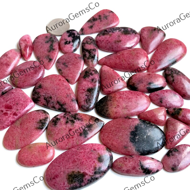 Puede incluir: Una colecci&oacute;n de 20 cabujones de piedras preciosas rosas y negras. Los cabujones son de varias formas y tama&ntilde;os, con un acabado liso y pulido. Las piedras tienen una base rosa con inclusiones negras.