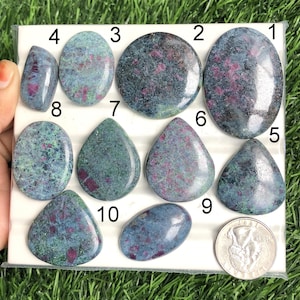 以下が含まれることがあります： 様々な形をした、研磨されたルビーゾイサイトの宝石10個のコレクション。楕円形、涙型、三角形など。石は緑、青、赤の色合いが混ざっており、サイズの参考として銀貨が添えられています。