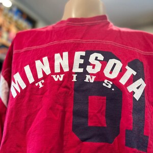 May include: Red long-sleeve t-shirt with white lettering that reads "Minnesota Twins" and a navy blue number "01" on the back.