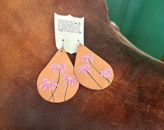 May include: A pair of leather earrings with pink flower designs. The earrings are teardrop shaped and have a silver hook.