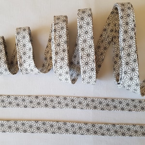 May include: White cotton ribbon with a black geometric pattern of stars. The ribbon is folded and laid out on a white surface.