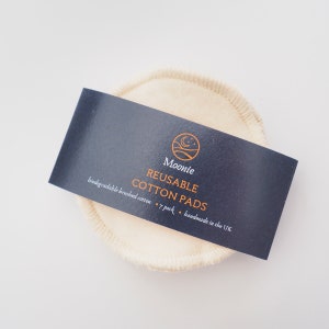 K&ouml;nnte beinhalten: Eine Packung mit 7 wiederverwendbaren Wattepads aus biologisch abbaubarer, geb&uuml;rsteter Baumwolle. Die Pads sind wei&szlig; und haben einen gen&auml;hten Rand. Die Verpackung ist schwarz mit wei&szlig;em Text, der "Moonie Reusable Cotton Pads 7 pack handmade in the UK" lautet.