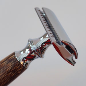 May include: A chrome safety razor with a wooden handle. The razor has a chrome head with a safety bar and a blade.