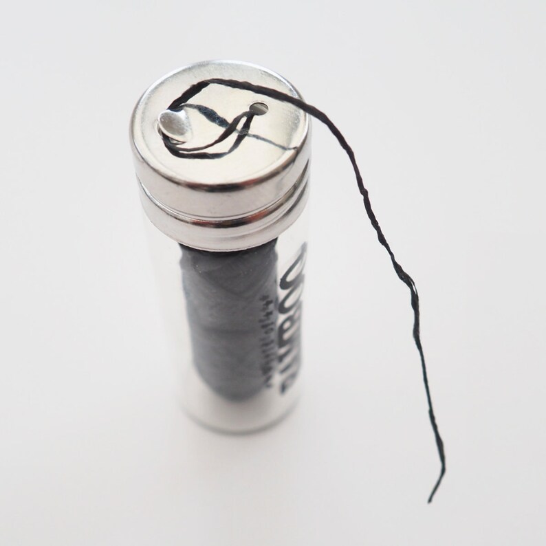 May include: A small glass jar with a silver lid containing black dental floss. The floss is pulled out of the jar and is hanging down.