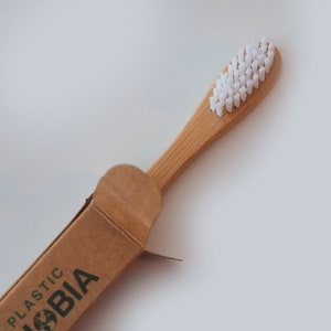 K&ouml;nnte beinhalten: Ein brauner Karton mit dem Aufdruck "PLASTIC PHOBIA". Die Schachtel ist ge&ouml;ffnet und eine Bambuszahnb&uuml;rste mit wei&szlig;en Borsten ragt teilweise heraus.