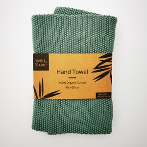 K&ouml;nnte beinhalten: Ein gr&uuml;nes, gestricktes Handtuch aus 100% Bio-Baumwolle. Das Handtuch misst 40 x 65 cm und hat ein braunes Etikett mit dem Text "Wild & Stone Hand Towel 100% Organic Cotton 40 x 65 cm Oeko-Tex Standard 100".