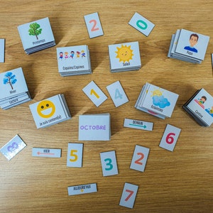 May include: A set of colorful cards with images and words in French. The cards include images of a sun, a cloud, a tree, a smiley face, and a person. The words on the cards include "Soleil", "Eclaircies", "Printemps", "Je suis content(e)", and "Papa". There are also number cards with the numbers 1, 2, 3, 4, 5, 6, 7, and 0.