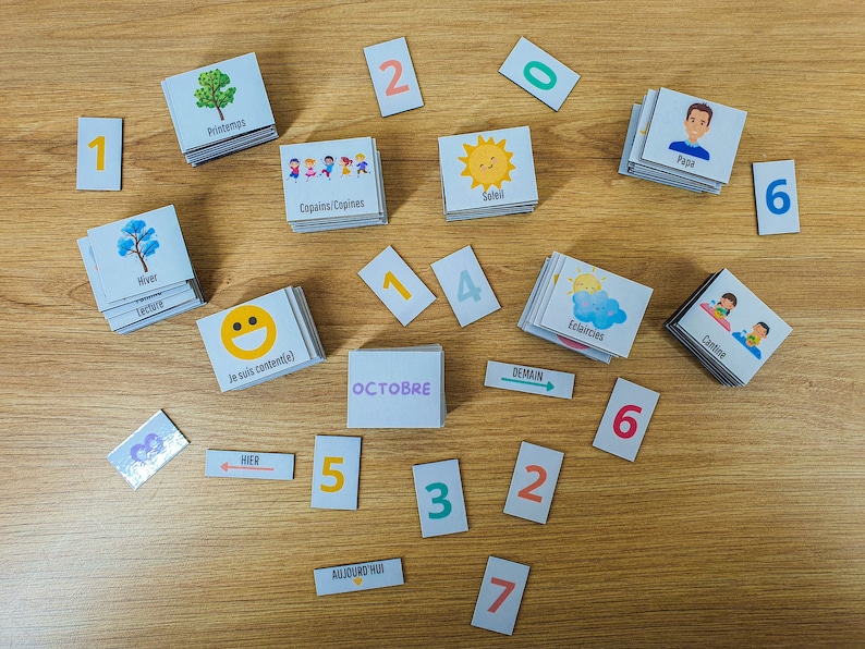 May include: A set of colorful cards with images and words in French. The cards include images of a sun, a cloud, a tree, a smiley face, and a person. The words on the cards include "Soleil", "Eclaircies", "Printemps", "Je suis content(e)", and "Papa". There are also number cards with the numbers 1, 2, 3, 4, 5, 6, 7, and 0.