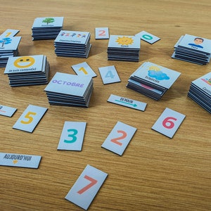 May include: A set of colorful cards with various images and text, including numbers, days of the week, and months. The cards are arranged on a wooden surface.