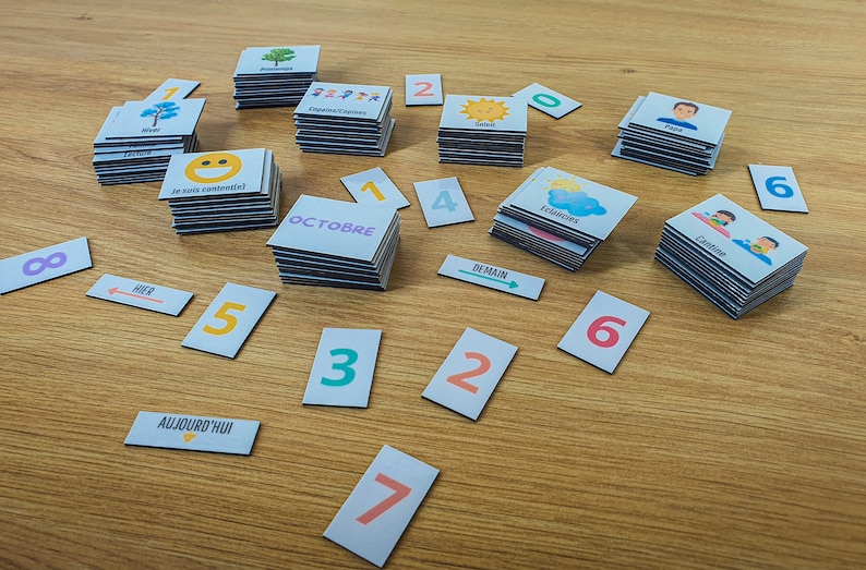 May include: A set of colorful cards with various images and text, including numbers, days of the week, and months. The cards are arranged on a wooden surface.