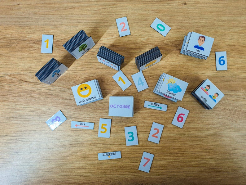 May include: A set of colorful magnetic cards for teaching children about days of the week, months, and numbers. The cards feature images of a smiling face, a cloud with a sun, a tree, a person, and the words "hier", "demain", "aujourd'hui", "octobre", and "eclecies".