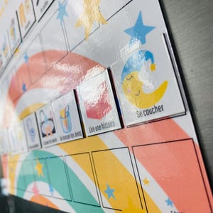 Może przedstawiać: Biała magnetyczna tablica rutynowa z kolorowym wzorem tęczy i gwiazd. Tablica zawiera kwadratowe ikony z francuskim tekstem, takim jak Se coucher, Lire une histoire i Se brosser les dents, wraz z ilustracjami księżyca oraz gwiazd.