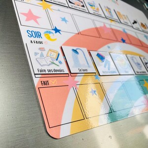 Może przedstawiać: Magnetyczna tablica obowiązk&oacute;w z motywem tęczy, gwiazd i księżyca. Tablica zawiera sekcje oznaczone jako SOIR A FAIRE i FAIT, z piktogramami zadań, takimi jak Faire ses devoirs, Se laver oraz Mettre le pyjama.