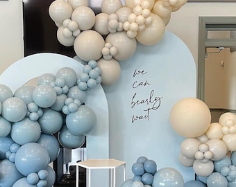 May include: A blue and white balloon arch with the text "we can barely wait" on a light blue backdrop. The balloons are arranged in a cascading pattern, creating a festive and celebratory atmosphere.