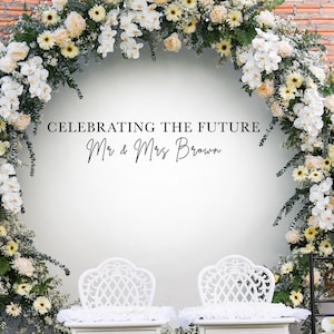 Può includere: Un muro bianco con un arco floreale fatto di fiori bianchi e gialli. Il testo "Celebrating the Future Mr. & Mrs. Brown" è scritto sul muro. Due sedie bianche sono posizionate davanti al muro.
