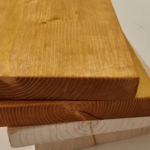 May include: Three wooden boards stacked on top of each other. The top board is stained a dark orange color, while the bottom two boards are a natural wood color.