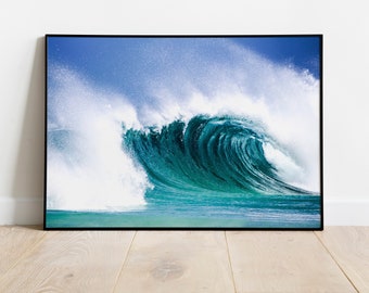 Puede incluir: Una impresión enmarcada de una gran ola oceánica. La ola es de un color turquesa vibrante, con espuma blanca y rocío. El cielo es de un azul claro. La impresión está en un marco negro y se muestra sobre un suelo de madera clara.
